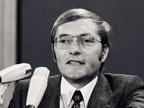Rudolf Augstein auf dem FDP-Parteitag am 23. Oktober 1972 Auf dem Schwarz-Weiß-Foto ist der Gründer von „Der Spiegel“, Rudolf Augstein, auf einem FDP-Parteitag 1972 in seiner Funktion als Delegierter des Landesverbandes Nordrhein-Westfalen zu sehen. Vor Augstein stehen drei Mikrofone. Er selbst trägt eine Brille mit Metallrahmen, einen dunklen Anzug mit Karomuster und eine schwarze Krawatte mit bunten Mustern.