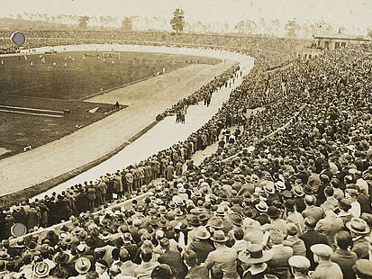 Schwarzweißfoto eines Stadions mit Fußballfeld und voll besetzten Sitzplatztribünen.
