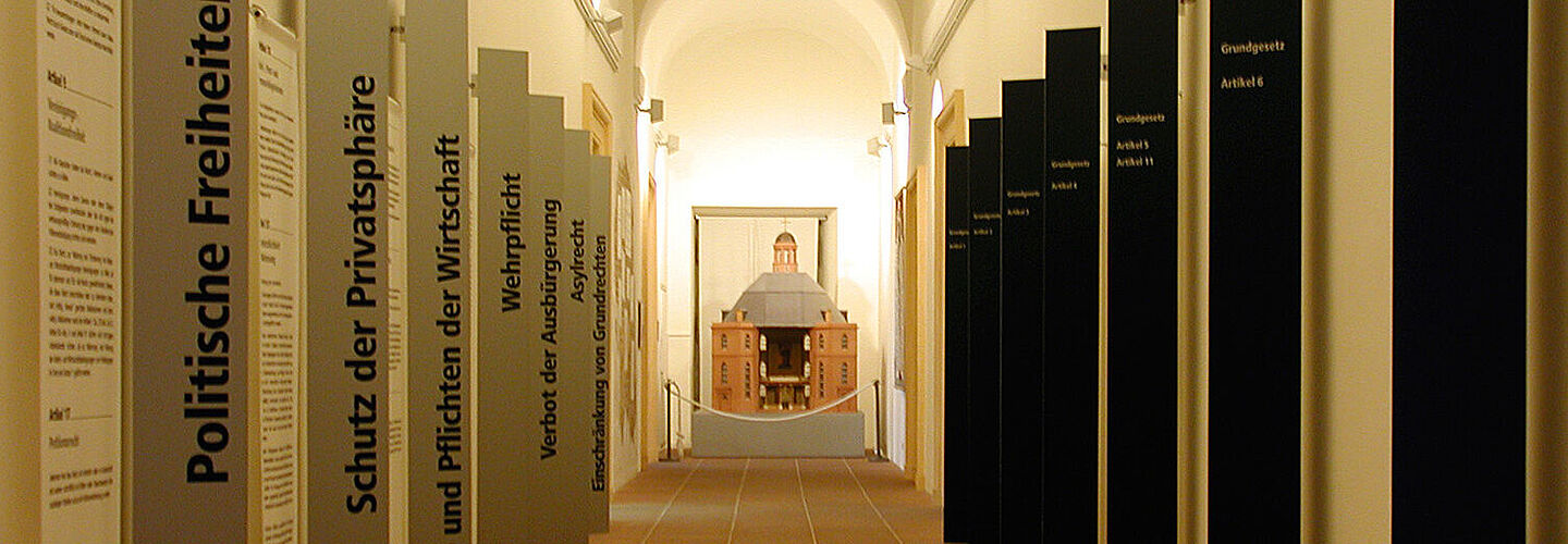 Ein langer Gang, der links und rechts gesäumt ist von Tafeln, auf denen die Grundrechte stehen. Am Ende des Gangs steht ein Modell von der Frankfurter Paulskirche.