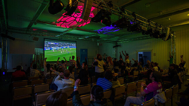 Leinwand mit der Live-Übertragung des EM-Eröffnungsspiels, jubelnde Zuschauerinnen und Zuschauer
