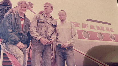 drei junge Männer stehen auf der Treppe, die aus einem Flugzeug der DDR-Fluggesellschaft Interflug führt.