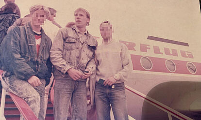 drei junge Männer stehen auf der Treppe, die aus einem Flugzeug der DDR-Fluggesellschaft Interflug führt.