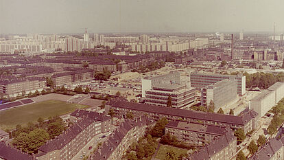 Farbige Luftaufnahme auf Häuser und einen Fußballplatz mit einer kleinen Tribüne.