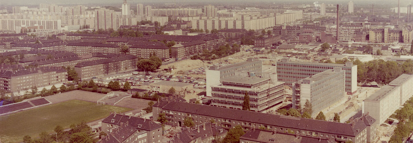 Farbige Luftaufnahme auf Häuser und einen Fußballplatz mit einer kleinen Tribüne.