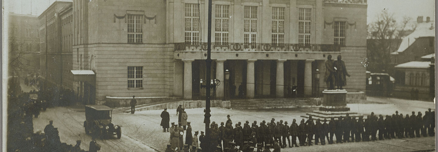 Schwarz-Weiß-Aufnahme einer Menschenschlange entlang der Vorderfront eines historischen Gebäudes