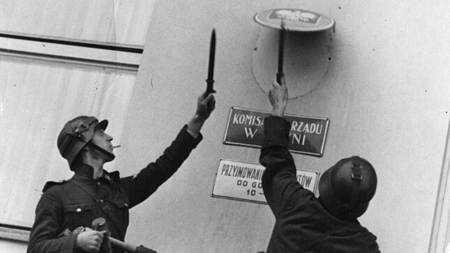 Schwarz-Weiß-Aufnahme mit zwei Soldaten beim Entfernen eines Schildes von einer Hausfassade