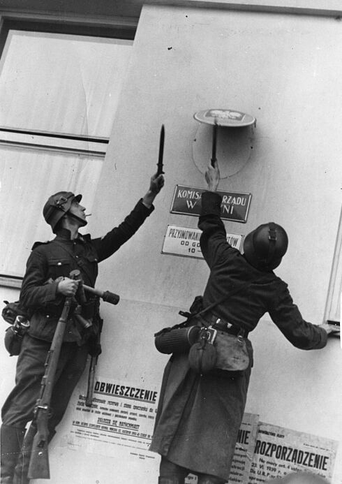 Schwarz-Weiß-Aufnahme mit zwei Soldaten beim Entfernen eines Schildes von einer Hausfassade