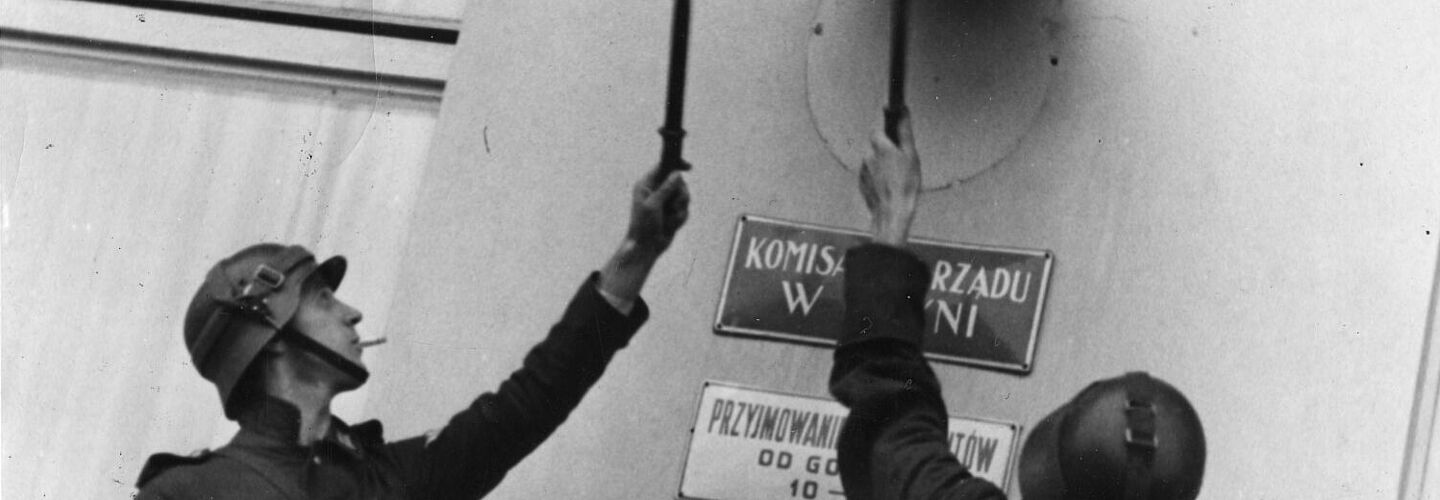 Schwarz-Weiß-Aufnahme mit zwei Soldaten beim Entfernen eines Schildes von einer Hausfassade