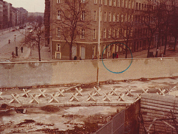 Blick von einer Besucherplattform in der Bernauer Straße auf Ost-Berlin. Vor einem Häuserblock steht eine kleine Gruppe von Menschen, die auf dem Foto in einem grünen Kreis markiert sind.
