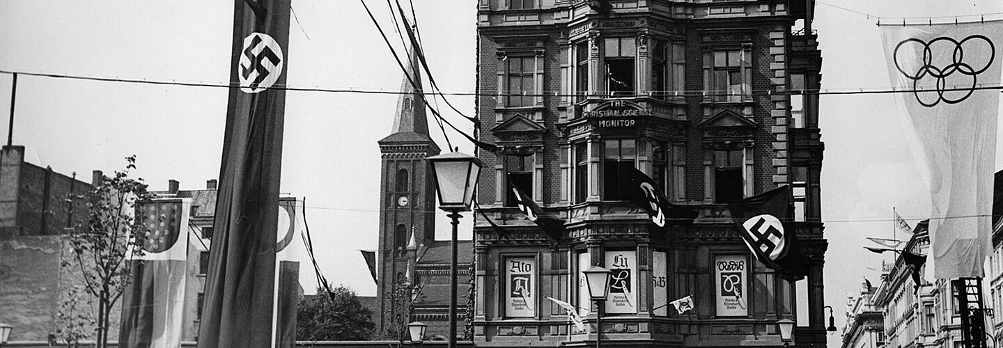 Straßenschmuck an der Straße „Unter den Linden“, Ecke Neustädtische Kirchstraße während der Olympischen Sommerspiele 1936 in Berlin