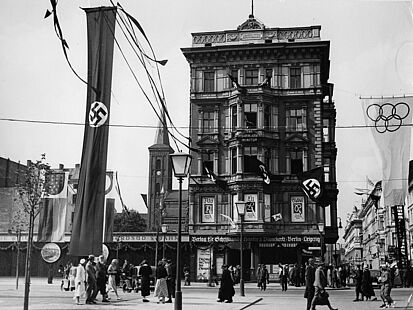 Straßenschmuck an der Straße „Unter den Linden“, Ecke Neustädtische Kirchstraße während der Olympischen Sommerspiele 1936 in Berlin