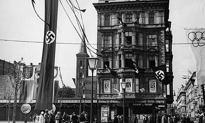 Straßenschmuck an der Straße „Unter den Linden“, Ecke Neustädtische Kirchstraße während der Olympischen Sommerspiele 1936 in Berlin