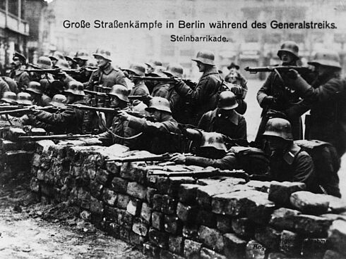 Schwarz-Weiß-Aufnahme von Soldaten hinter einer Steinmauer mit Gewehren im Anschlag