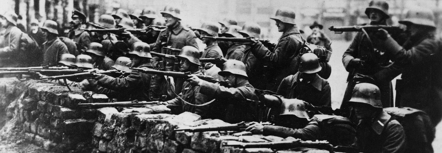 Schwarz-Weiß-Aufnahme von Soldaten hinter einer Steinmauer mit Gewehren im Anschlag