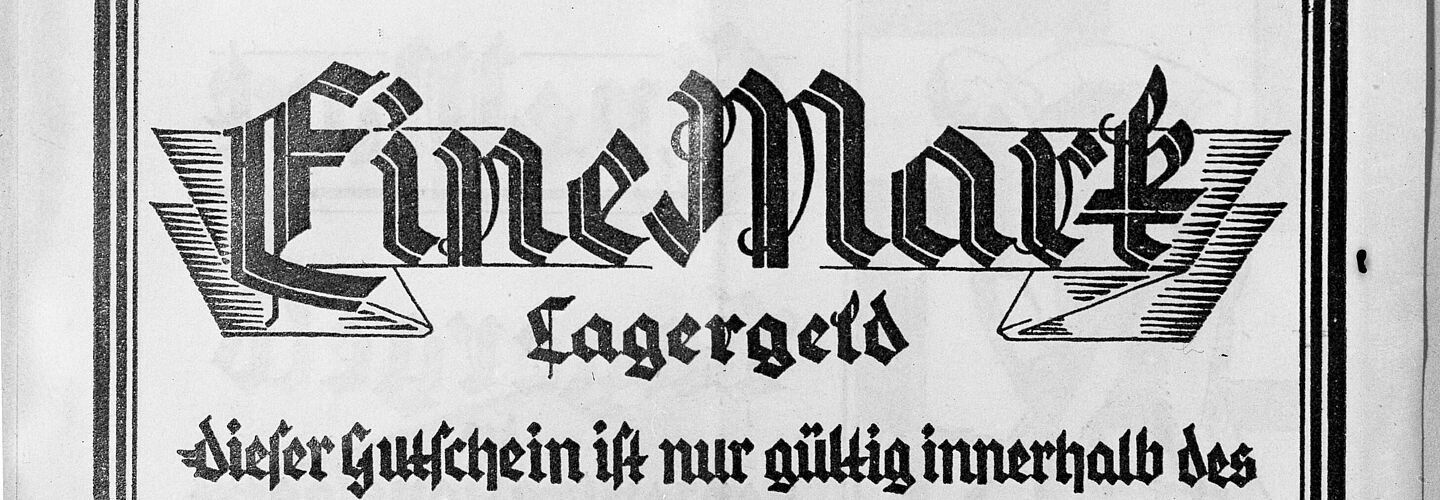 Abgebildet sind zwei Wertmarken des sogenannten "Lagergeld", welches den Inhaftierten eines Konzentrationslagers als Währung dienen sollte. Die obere Bildhälfte wird von einer 50 Pfennig-Marke eingenommen.