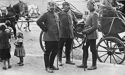 Drei preußische Offiziere stehen vor einer Kutsche.