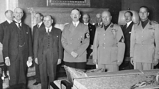 Schwarz-Weiß-Aufnahme mit sieben Männern in Anzügen und drei Männern in Uniform in einem mondän eingerichteten Raum