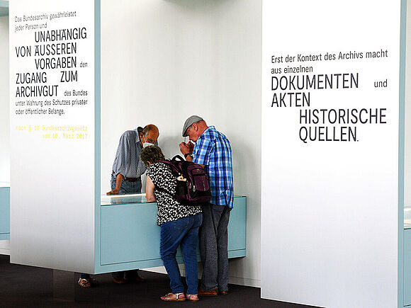 Besucherinnen und Besucher betrachten eine Vitrine in der Dauerausstellung „Geschichte in Geschichten“.