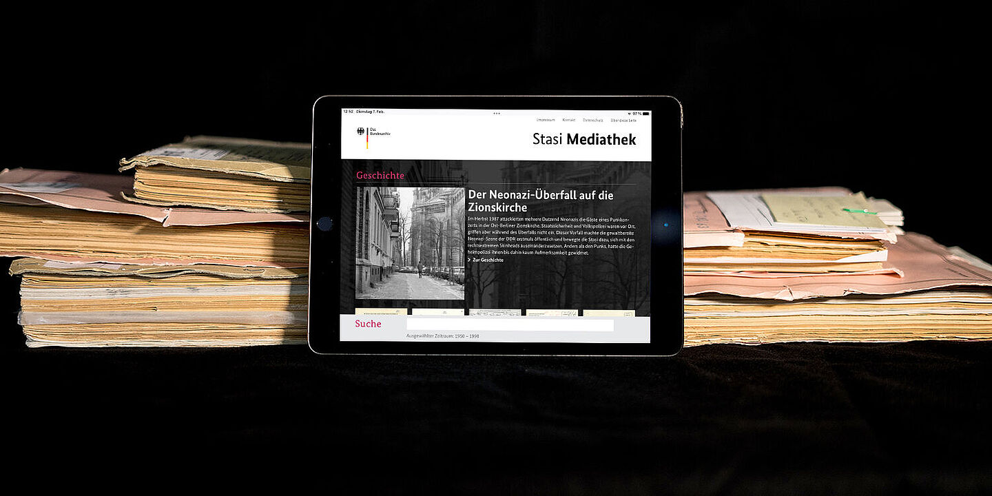 Stasi-Mediathek Das Bild zeigt die auf einem Tablet geöffnete Startseite der Stasi-Mediathek. Das Tablet lehnt an einigen Aken., Quelle:
BStU / Mulders