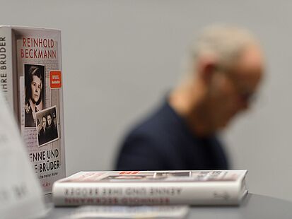 Zu sehen sind mehrere Bücher mit dem Titel "Aenne und ihre Brüder". Im Hintergrund sieht man im Profil den Autor Reinhold Beckmann.