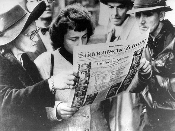 Mehrere Frauen und Männer lesen eine Sonderausgabe der „Süddeutschen Zeitung“, die über die Urteilsverkündung im Nürnberger Prozess informiert. Auf dem Titelblatt sind die Angeklagten zu sehen.