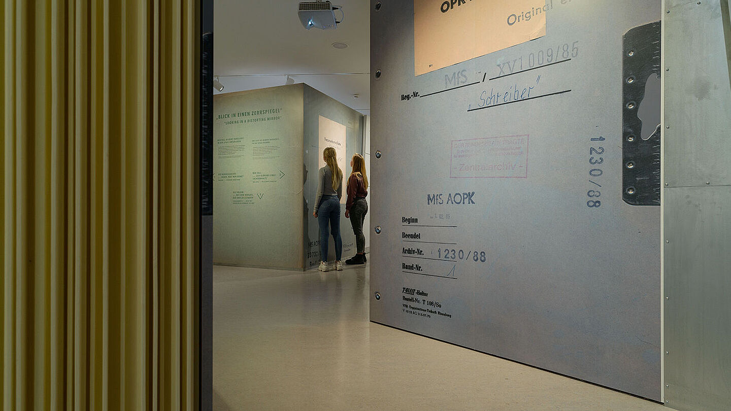 Das Bild zeigt zwei Personen in der Ausstellung Einblick ins Geheime. Sie stehen vor einem großen Aktenblatt, Quelle:
            BStU/Dresen
