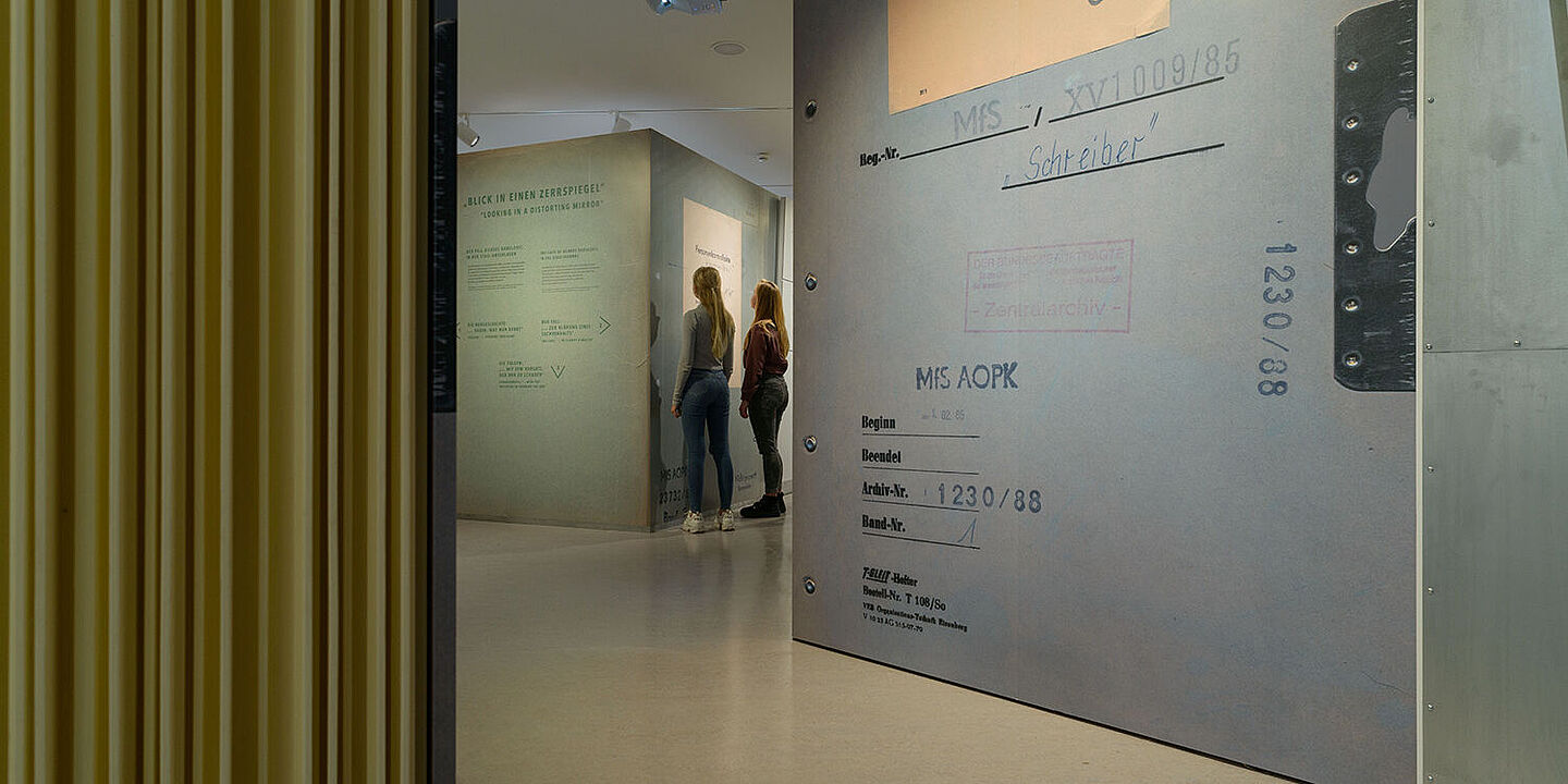 Das Bild zeigt zwei Personen in der Ausstellung Einblick ins Geheime. Sie stehen vor einem großen Aktenblatt, Quelle:
            BStU/Dresen