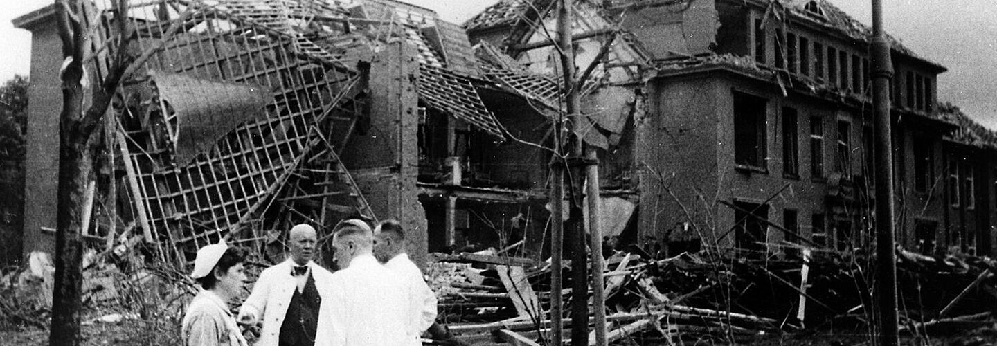 Ruinen des Krankenhauses Hamburg-Barmbeck, im Vordergrund stehen drei Ärzte und eine Krankenpflegerin im Gespräch