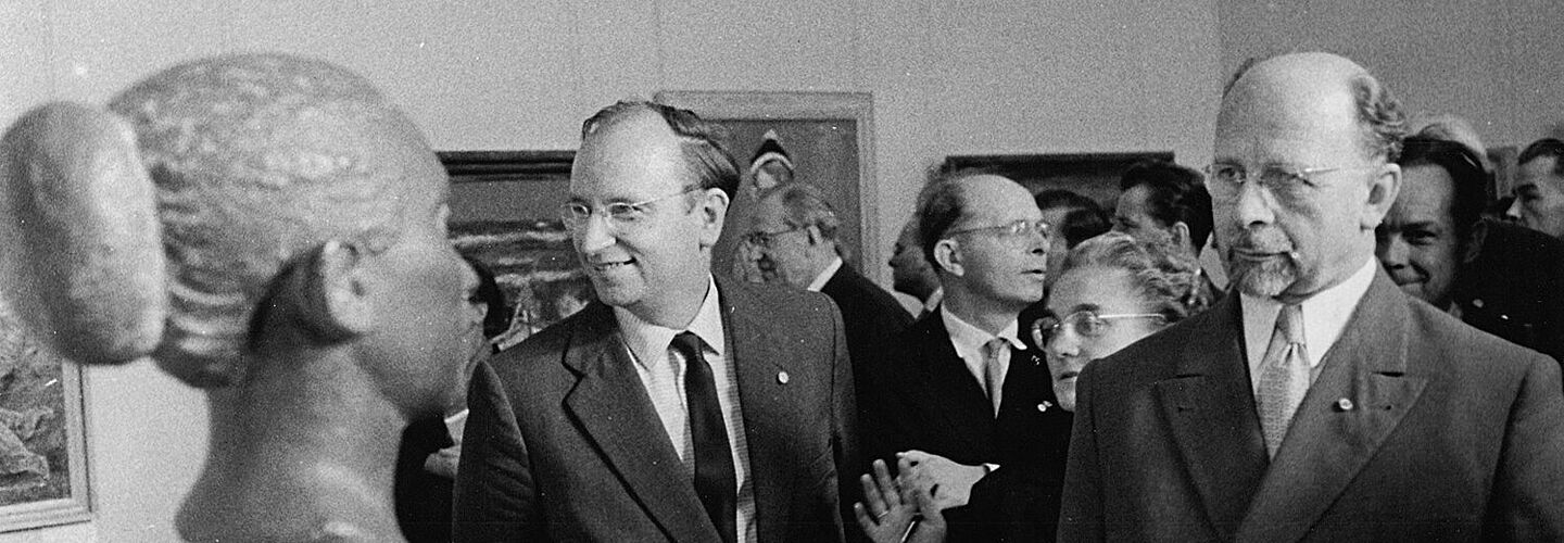 Walter Ulbricht und Kurt Hager blicken auf eine Skulptur, die einen Kopf mit Haarknoten darstellt.