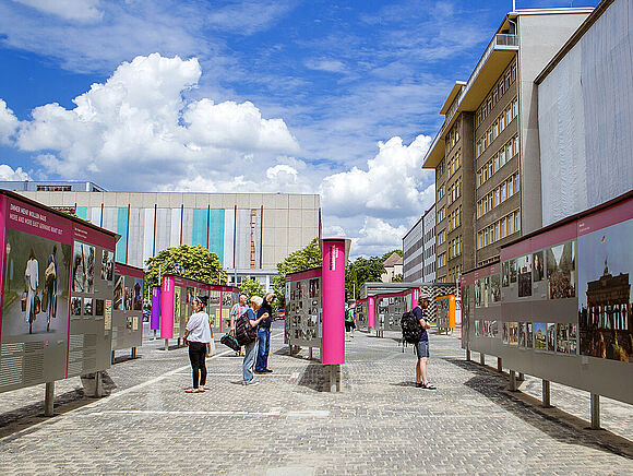 Das Bild zeigt Menschen, die sich im Innenhof der „Stasi-Zentrale. Campus für Demokratie“ die Open-Air-Ausstellung „Revolution und Mauerfall“ ansehen
