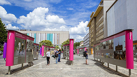 Das Bild zeigt Menschen, die sich im Innenhof der „Stasi-Zentrale. Campus für Demokratie“ die Open-Air-Ausstellung „Revolution und Mauerfall“ ansehen