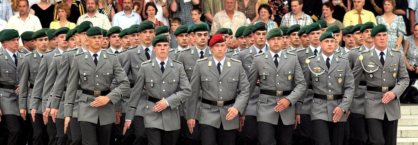 Mehrere Bundeswehrsoldaten marschieren. Im Hintergrund sind Zuschauerinnen und Zuschauer zu sehen.