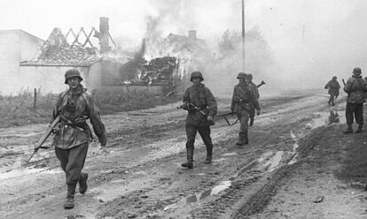 Deutsche Soldaten auf einer Straße vor brennenden Gebäuden.