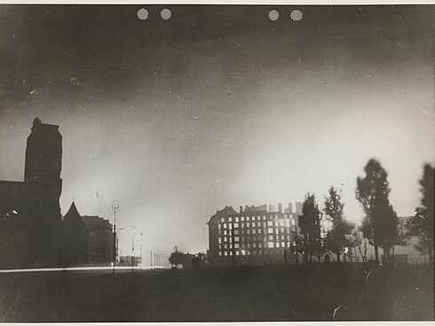 Nachtaufnahme vom brennenden Warschau, auf der Ruinen und Bäume zu sehen sind.