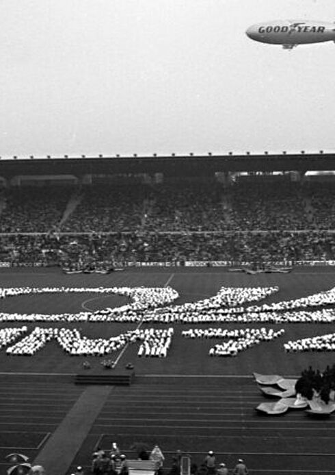 Schulkinder bilden auf dem Rasen das WM-Logo Stadion mit einer WM-Logo-Formation aus Kindern auf dem Rasen; Zeppelin schwebt über das Spielfeld
