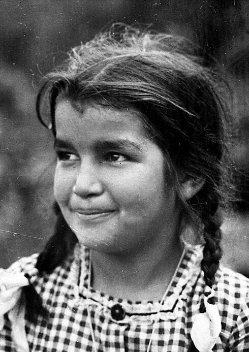 Schwarz-Weiß-Porträtaufnahme eines lächelnden Mädchens mit geflochtenen Zöpfen und kariertem Oberteil