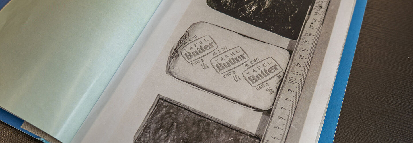 Ein Foto einer aufgeschlagenen Beispielakte. Zu sehen sind ein Stück verpackte Butter und daneben zwei Blöcke gleicher Größe. Am unteren Bildrand ist ein Maßstab angelegt.