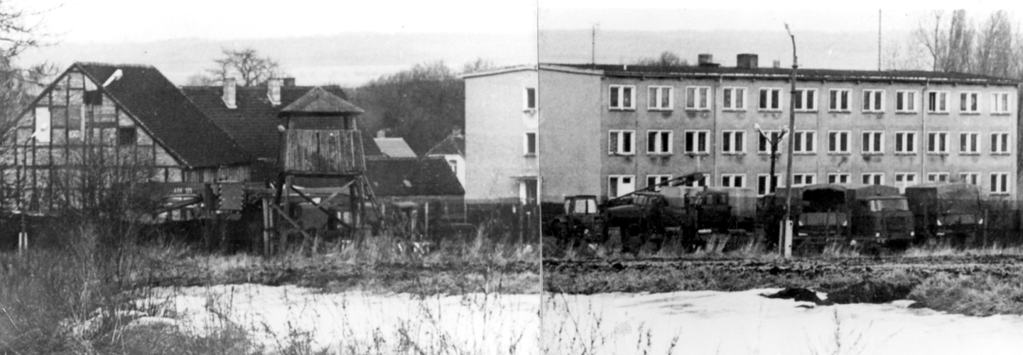 [Das abgebildete schwarzweiße Lichtbild ist ein aus drei Fotos zusammengestelltes Panoramabild. Hinter schneebedeckter Freifläche ist abgezäuntes Gelände. Links steht ein Fachwerkgebäude, direkt rechts daneben ein hölzerner Aussichtsturm. In der Bildmitte ist ein dreistöckiges, langgestrecktes helles Gebäude mit Flachdach. Es folgt rechts daneben ein weiteres, etwas niedrigeres Gebäude mit Spitzdach, das aber hinter kahlen Laubbäumen schlechter erkennbar ist. Vor den Gebäuden sind, vermutlich militärische, Planenfahrzeuge aufgereiht.]
