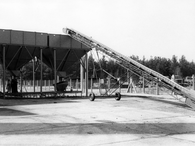 Das Schwarz-Weiß-Bild zeigt zeigt zwei trichterförmige, grosse Behältnisse. An einem dieser Behältnisse ist ein Förderband angebracht.