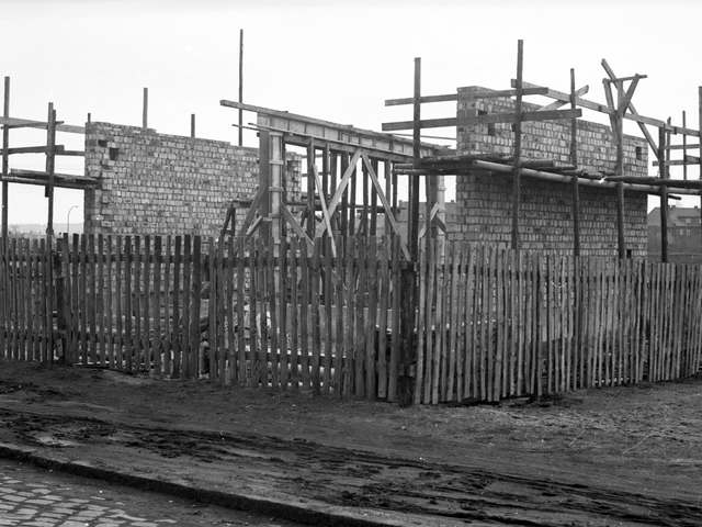Schwarz-Weiß-Aufnahme von eingerüsteten Außenmauern eines im Bau befindlichen Hauses in einer Wohngegend im ehemaligen Bezirk Halle. Das Baugelände ist von einem Holzlattenzaun umgeben.