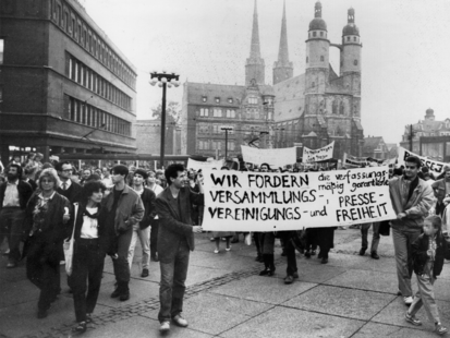 [Zu sehen sind viele Menschen auf dem Marktplatz in Halle. Zwei Männer tragen ein Transparent mit Aufschrift "Wir fordern die verfassungsmäßig garantierte Versammlungs-, Vereinigungs- und Pressefreiheit".M Es handelt sich um ein schwarzweißen Lichtbild.]