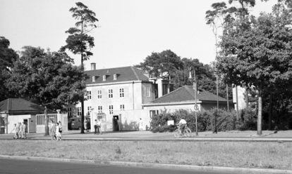 DAs Schwarz-Weiß-BIld zeigt den Sitz der US-Mission in der West-Berliner Clayallee: Aus dem geöffneten Tor gehen einige Menschen. Das Foto wurde von der Straße aus aufgenommen.