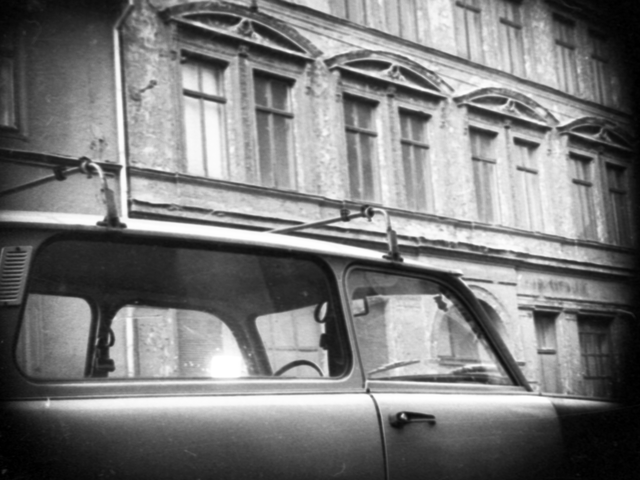 Über einen parkenden Trabant hinweg wurde mit versteckter Kamera ein Gebäude mit Fassadenstuck über den Fenstern des 1. Stocks fotografiert. 