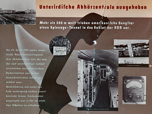 Unterirdische Abhörzentrale ausgehoben  Mehr als 300 m weit trieben amerikanische Gangster einen Spionage-Tunnel in das Gebiet der DDR vor.  Am 22.April 1956 legten sowjetische Nachrichtentruppen den Abhörstollen frei, der von der auf westberliner Gebiet errichteten amerikanischen Radarstation aus in den demokratischen Sektor gewühlt war. Heimtückisch, sich unter der Erde verbergend, hatten amerikanische Spione Telefonkabel angezapft, um so für sie wichtige Angaben zu erhalten.  [Der Hintergrund des vermeintlichen Flugblattes ist der Umriss eines alten Telefonhörers sowie kleine schwarz-weiße Aufnahmen aus dem Tunnel zu sehen. Es verläuft eine vertikale Risskante.]