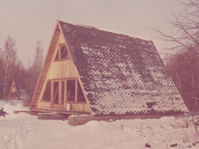 [Das Farbfoto zeigt drei versetzt angeordnete Finnhütten, die umgeben sind von einer schneebedeckten Landschaft und Bäumen. Die Frontflächen der Hütten sind holzgetäfelt und mit Türen und Fenstern versehen. Vor der vorderen Hütte ist ein Anhänger abgestellt, der an eine Feldküche erinnert.]