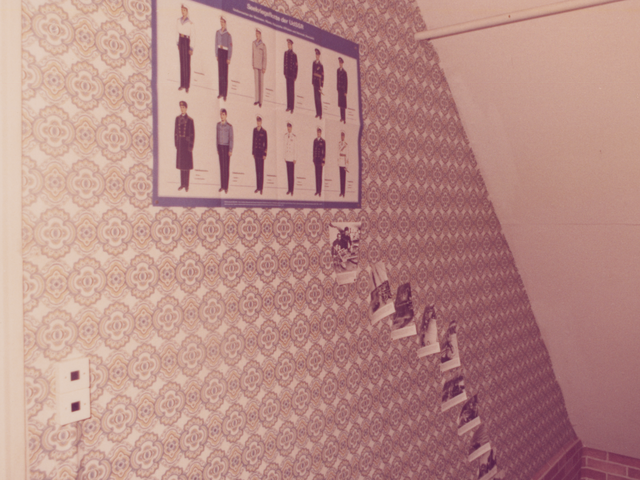 [Die Farbaufnahme zeigt den Bereich eines Treppenabgangs. Am oberen Teil der Seitenwand hängt ein Plakat mit der Überschrift "Seekriegsflotte der UdSSR". Darauf abgebildet sind zwölf gezeichnete Männer in unterschiedlichen Uniformen sowie jeweils eine kurze Beschreibung. Unter dem Plakat sind stufig angeordnete Fotografien mit darunterstehenden Texten angebracht.]