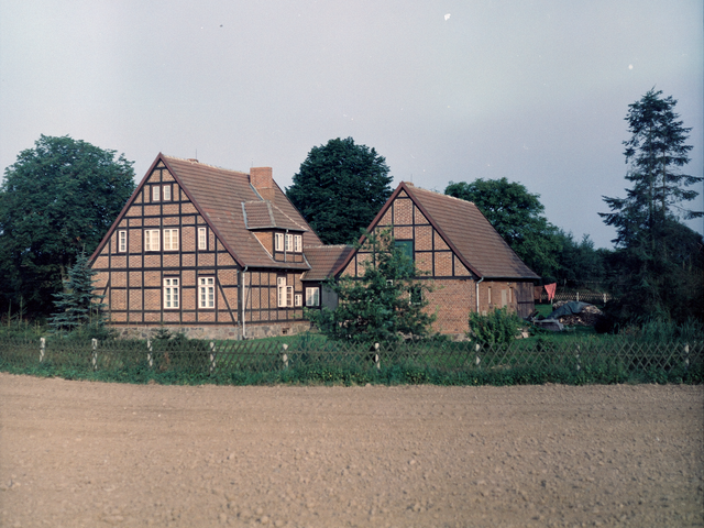 [Aufnahme zweier miteinander verbundener Fachwerkhäuser. Auf der Farbaufnahme lassen sich im Garten auch ein abgedeckter Holzhaufen swoei eine Wäscheleine erkennen.]
