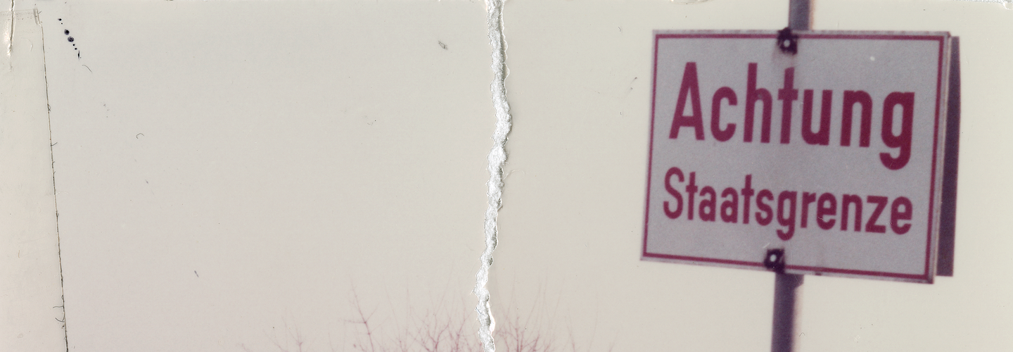 Das zerrissene und wiederhergestellte Bild zeigt den Blick in eine schneebedeckte Winterlandschaft. Dort steht ein Schild: "Achtung Staatsgrenze" 