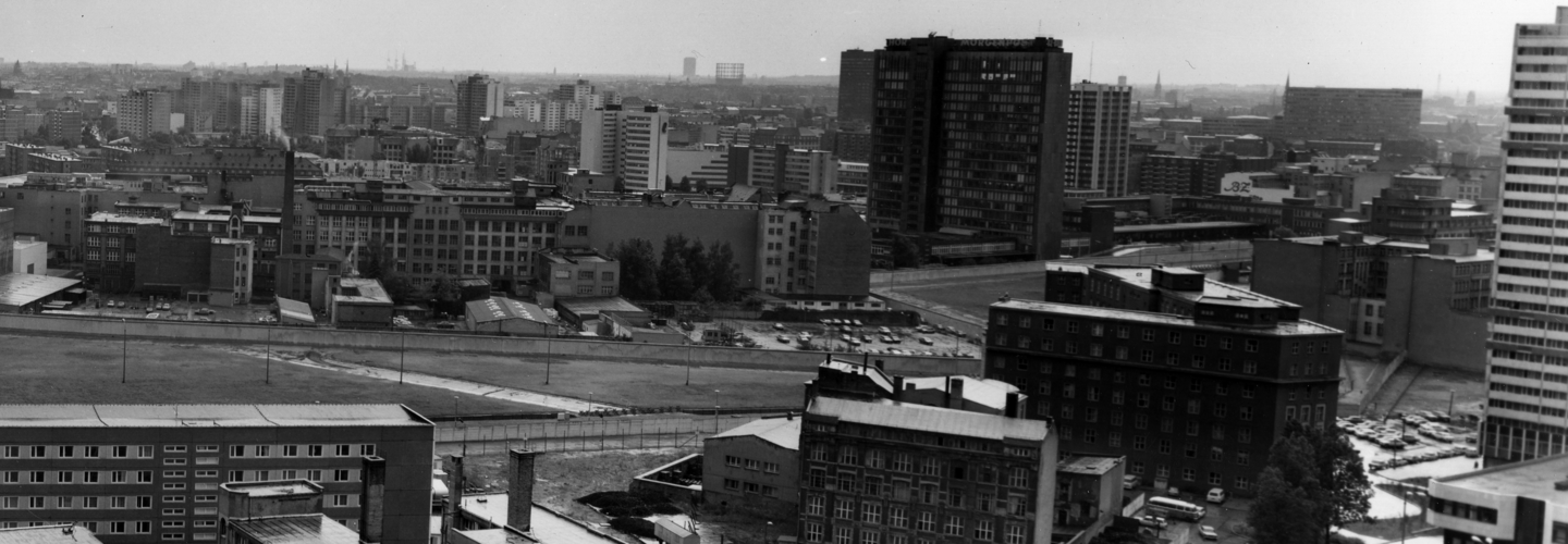 Foto vom Grenzverlauf in Berlin. Im Hintergrund ragt das Axel-Springer-Hochhaus empor.