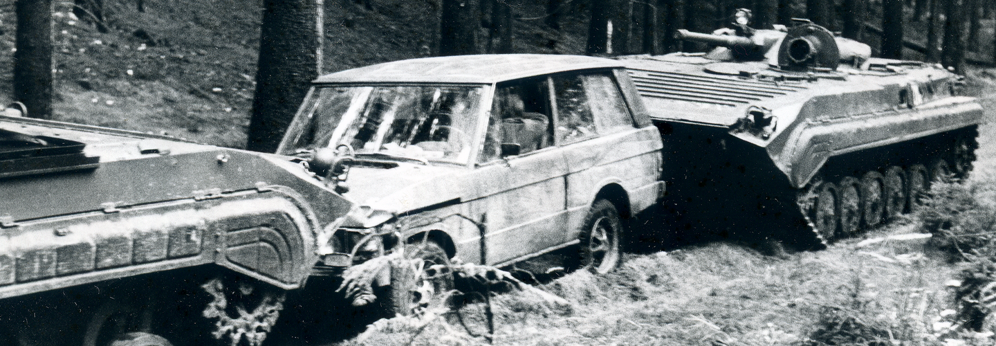 Das Bild zeigt einen von zwei Panzerwagen eingekeilten Jeep auf einem Waldweg.